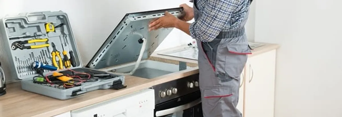 Cooktop repair technician lifting a built-in stovetop for service in Hialeah, FL